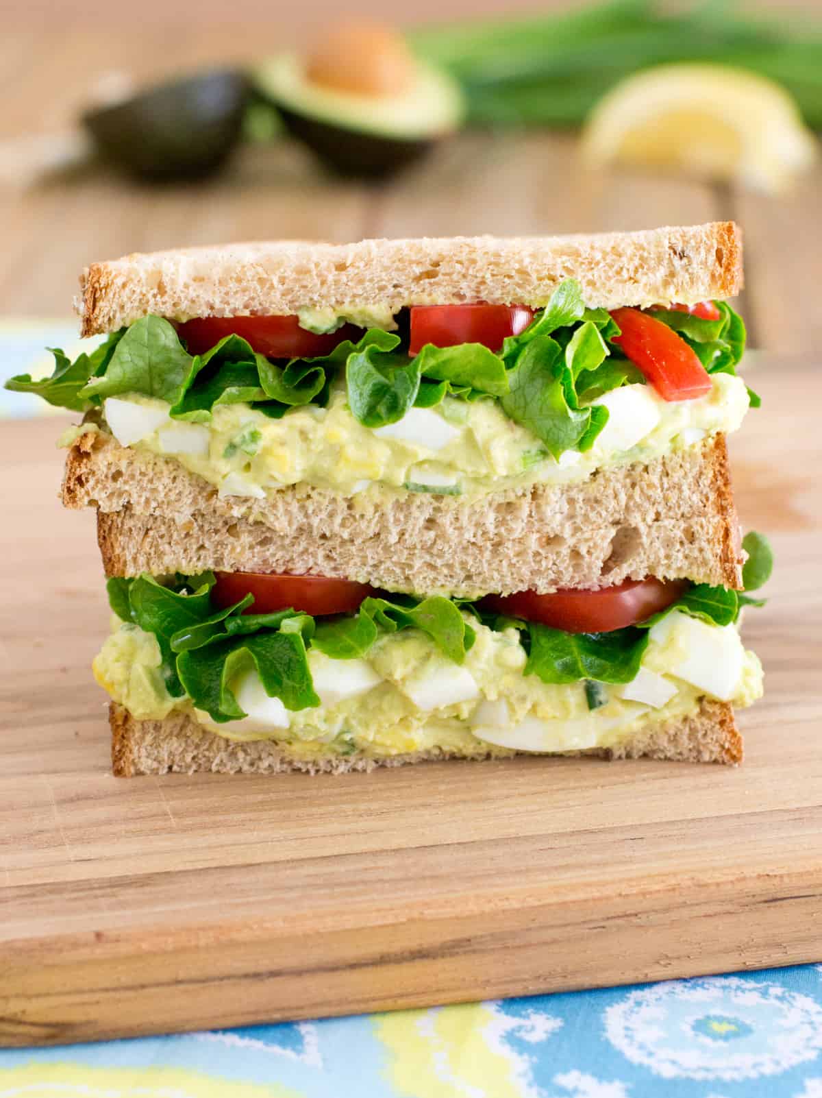 Avocado egg salad sandwich stacked on cutting board. 