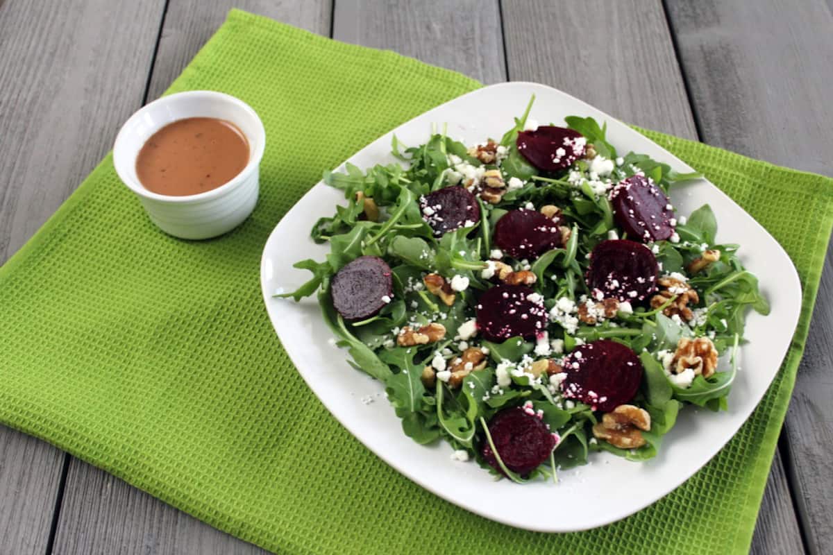 Beet, Goat Cheese and Walnut Salad on white plate with salad dressing. 