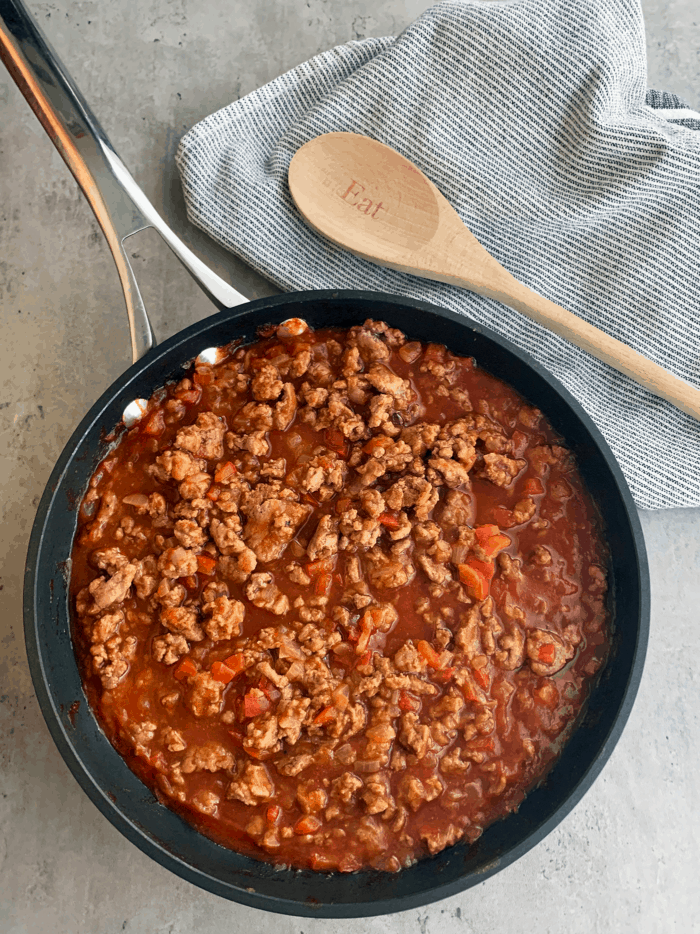 Skillet full of sloppy joes filling with wooden spoon and towel in background.