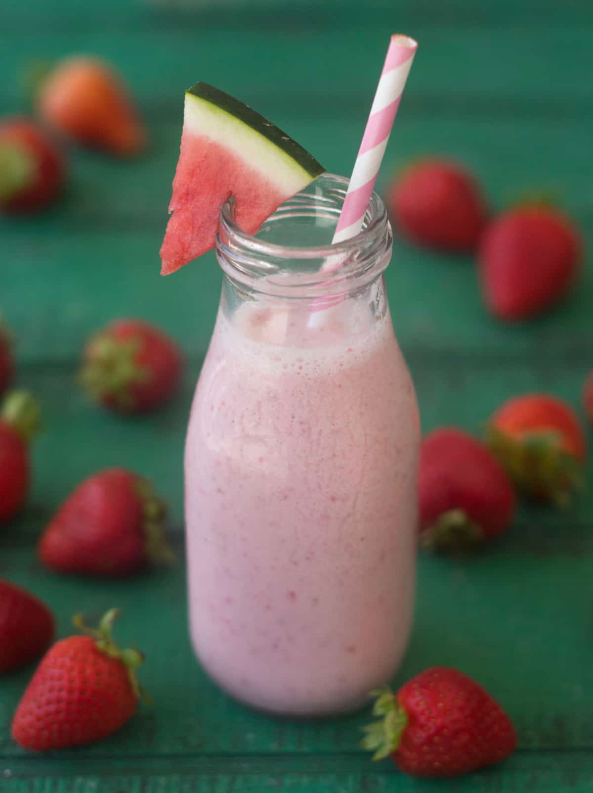 Fruit smoothie in jar with pink straw and watermelon wedge. 