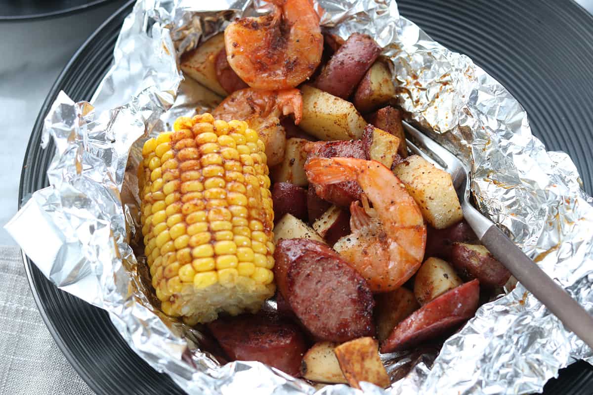 Top down view of foil packet opened up with shrimp boil meal inside, including shrimp, sausage, potatoes and corn on the cob.
