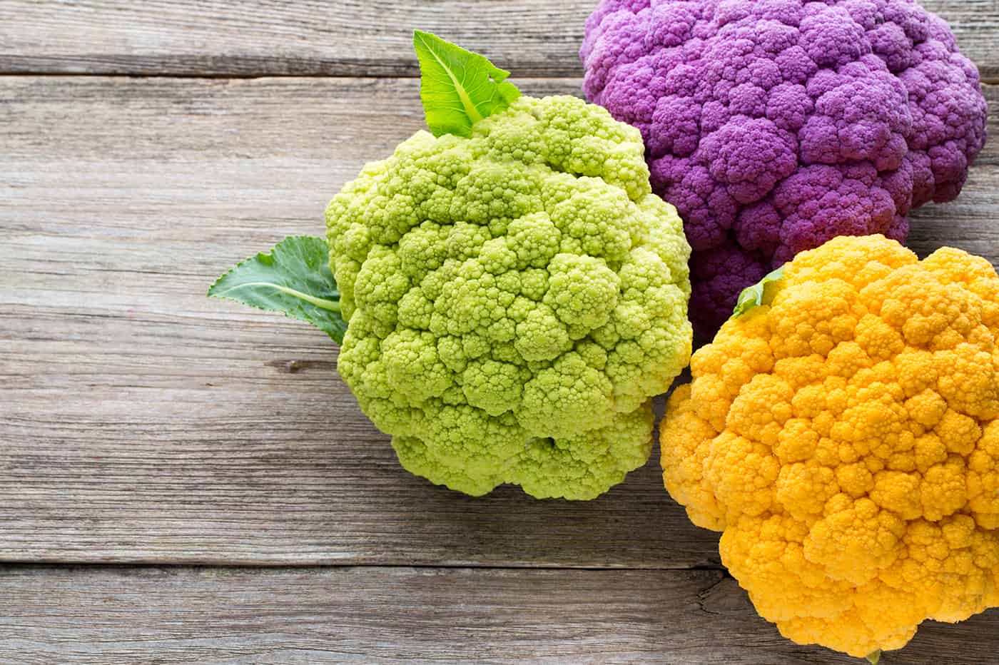 Rainbow of organic cauliflower on the wooden table.