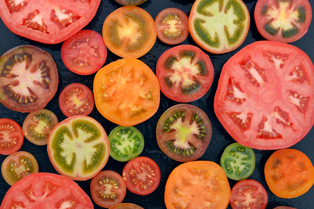 Different varieties of tomatoes sliced on black background