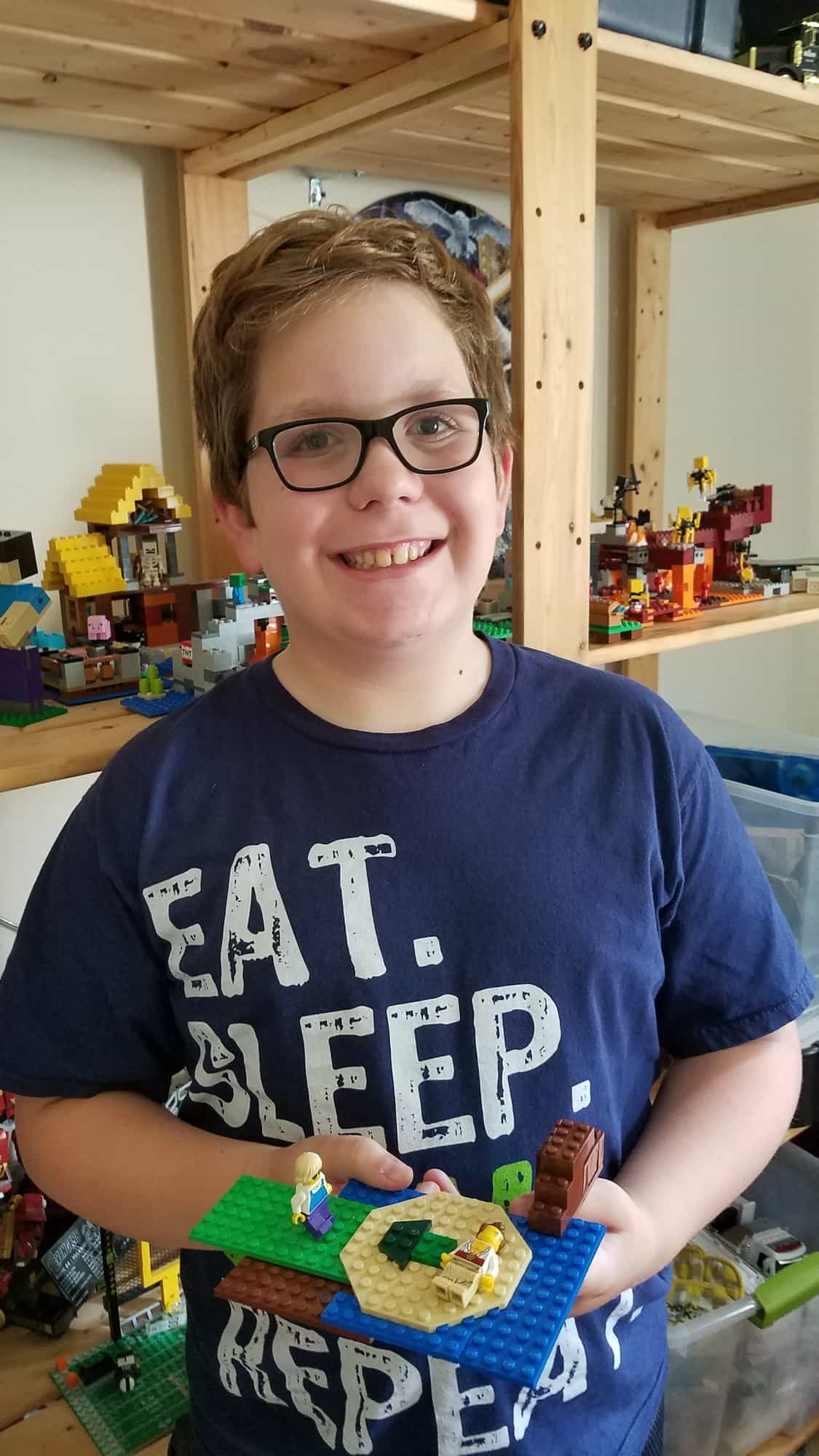 Smiling boy wearing glasses, proudly holding a creative LEGO construction