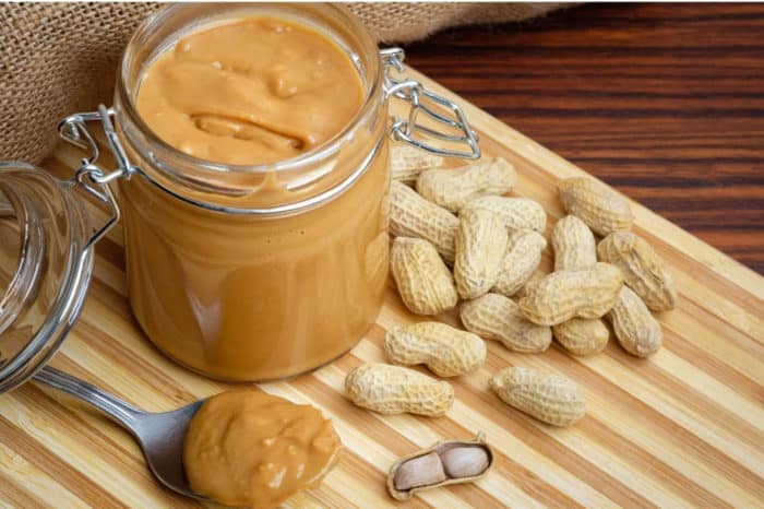 Peanut butter in jar on cutting board with peanut scattered