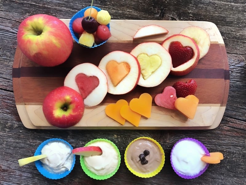 Fruit and cheese cut into shapes on cutting board with assorted dips