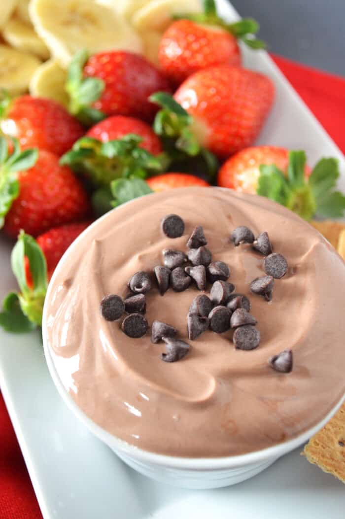 Bowl of chocolate yogurt fruit dip plated with strawberries and sliced bananas.