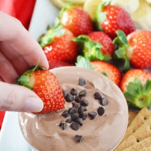 Hand dipping strawberry into a bowl of chocolate yogurt dip/