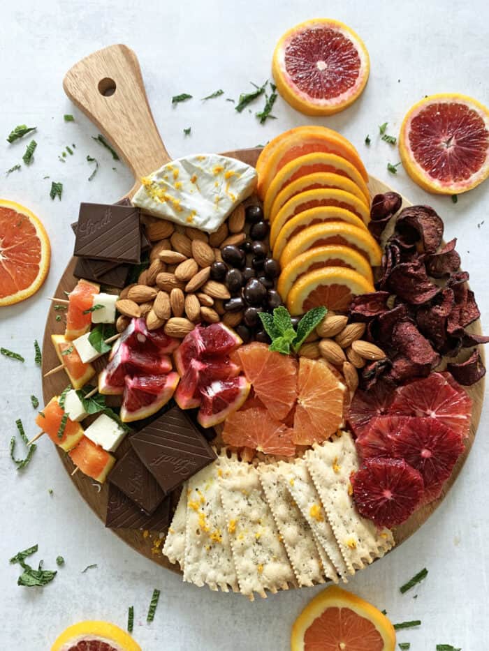 Grazing board with fresh citrus, chocolate, cheese, crackers, almonds, beet chips and more.