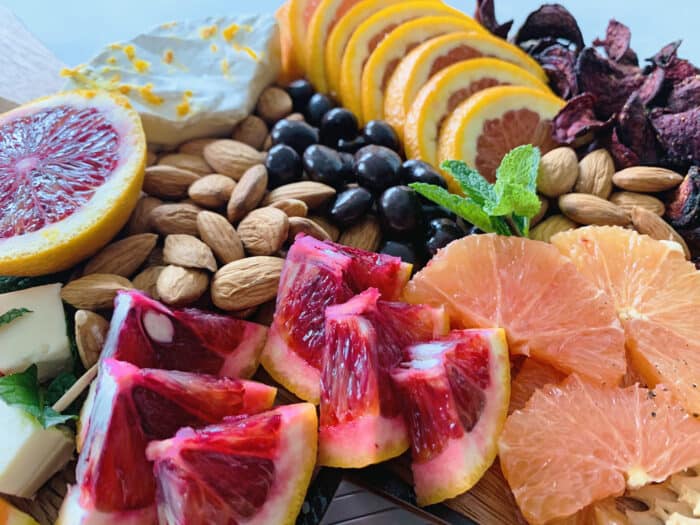 Close up of grazing board focusing on slices of blood oranges and cara cara oranges with almond and chocolate in the background.