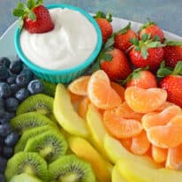 Cream cheese fruit dip in bowl plated with blueberries, kiwi, yellow apples, mandarins and strawberries.