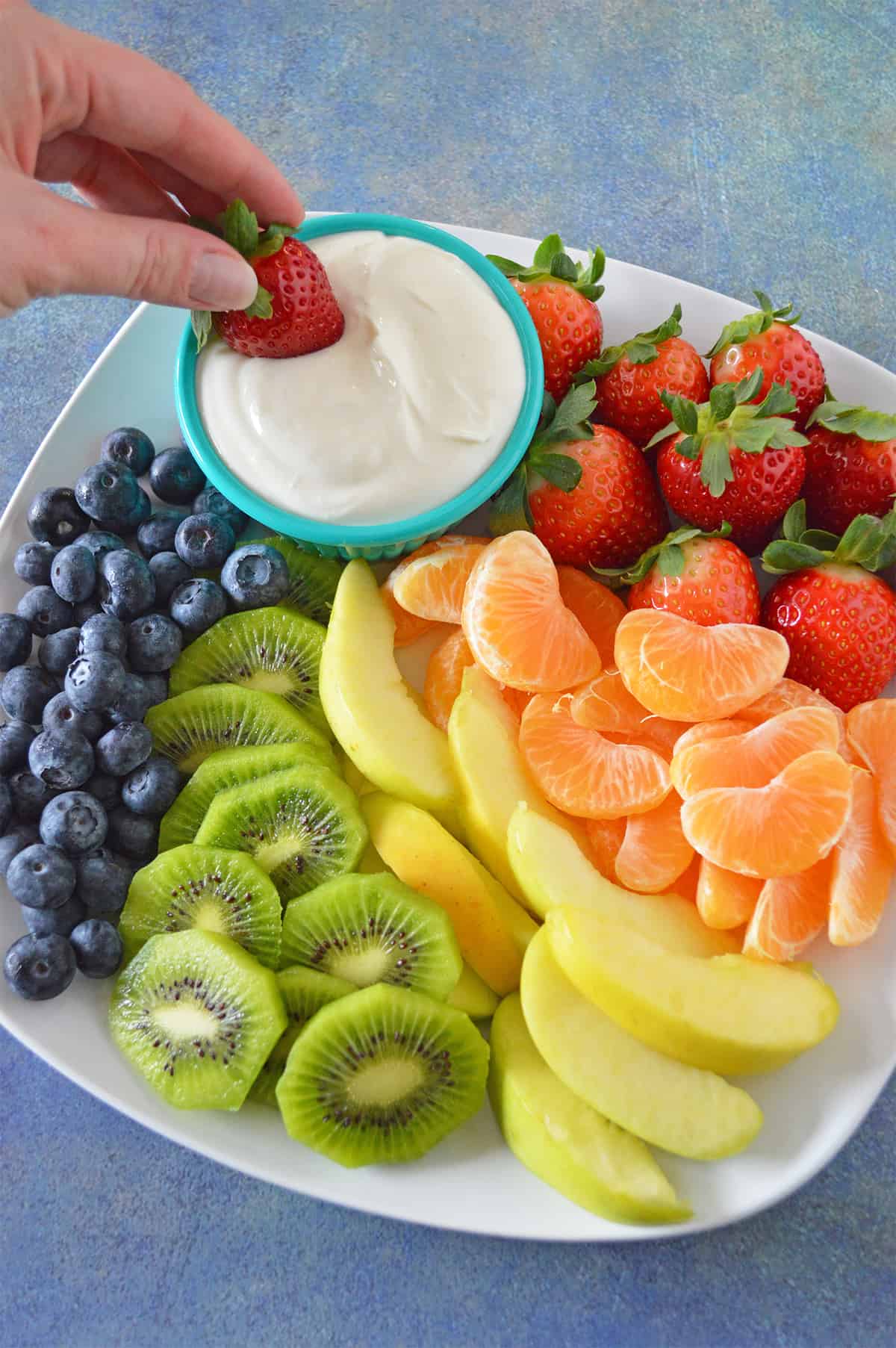 Hand dipping strawberry into cream cheese fruit dip.