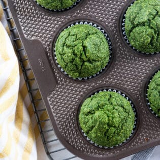 Overhead of green spinach muffins in muffins tin with yellow striped napkin.