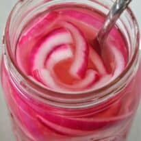 Close up of an open mason jar with pickled red onions and a fork.