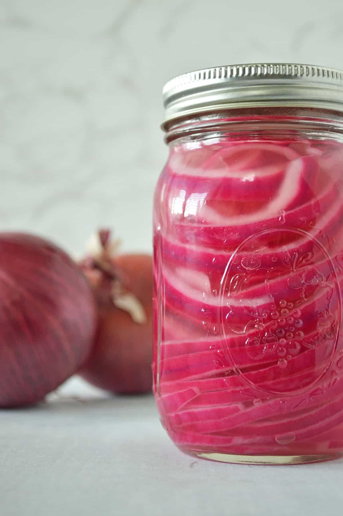 Mason jar filled with pickled red onions. Two large whole red onions in the background.
