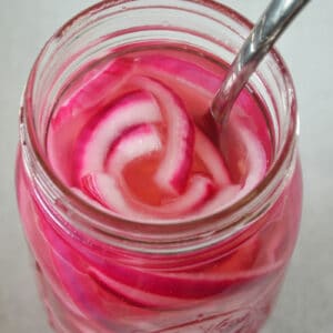 Close up of an open mason jar with pickled red onions and a fork.