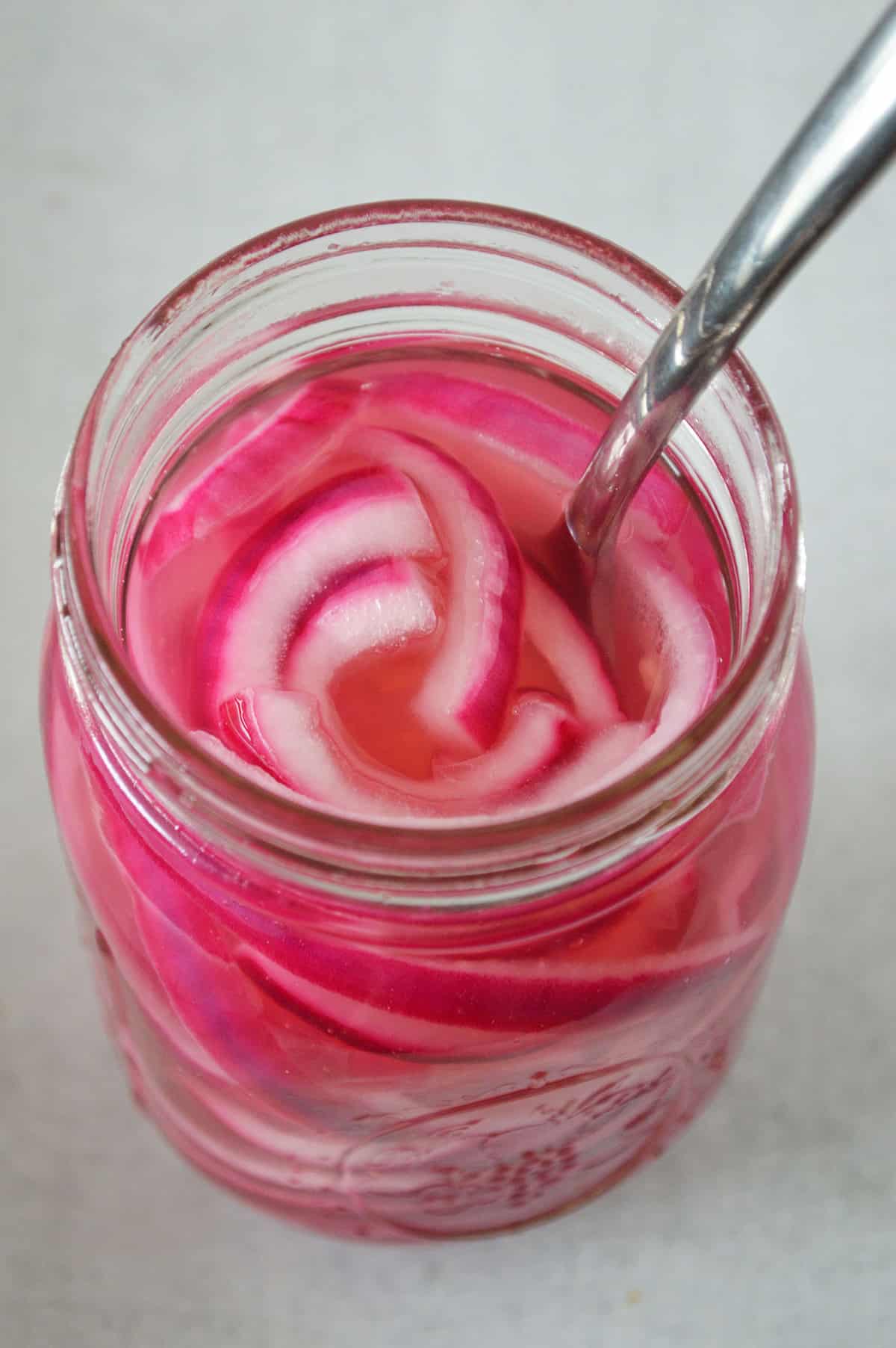 Close up of an open mason jar with pickled red onions and a fork.