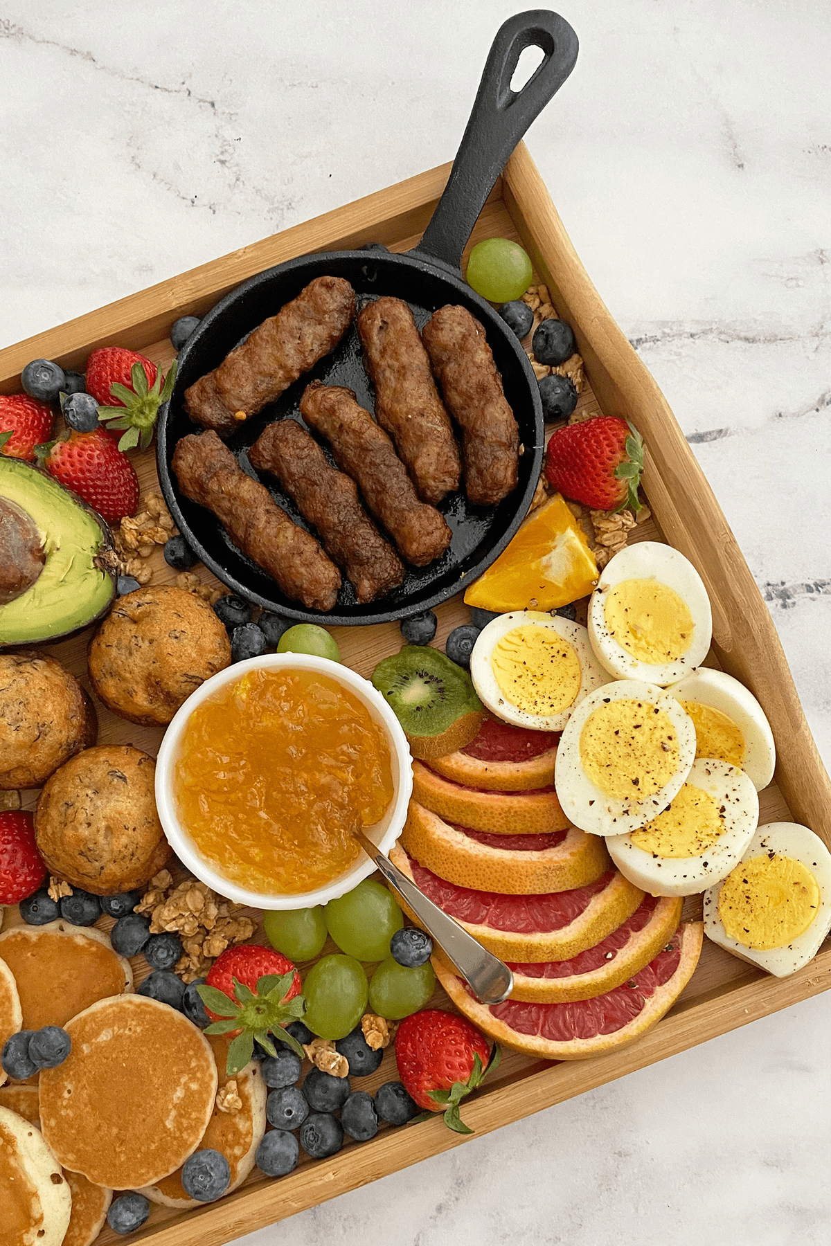 Close up of breakfast grazing board focusing on sausage links, hard-boiled eggs and fruit.