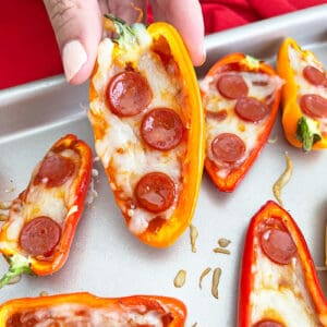 Close up of hand picking up mini pepper pizza off baking sheet.