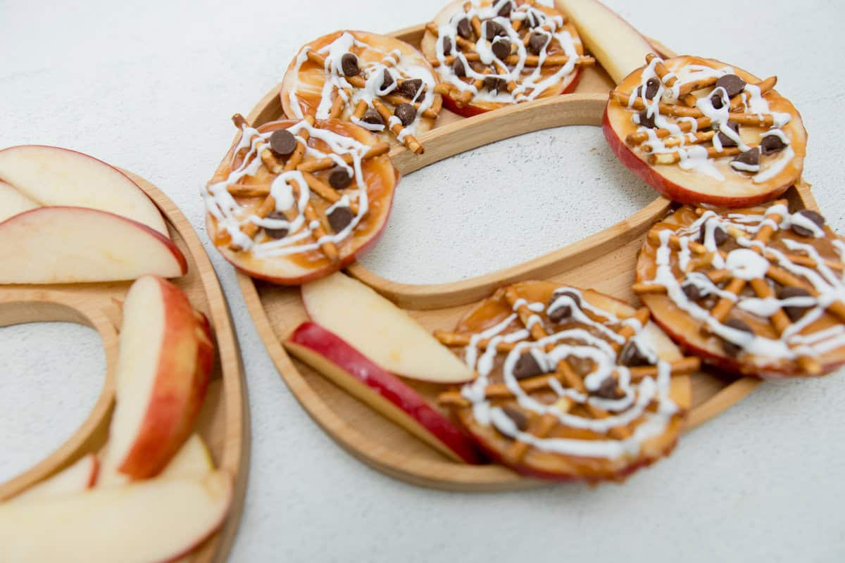 Apple round slices topped with pretzels and chocolate chips simulating spider webs.