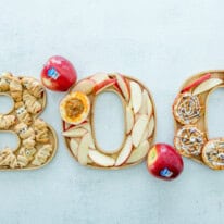 Halloween board spelling BOO with apple slices, cinnamon rolls, and mummies.