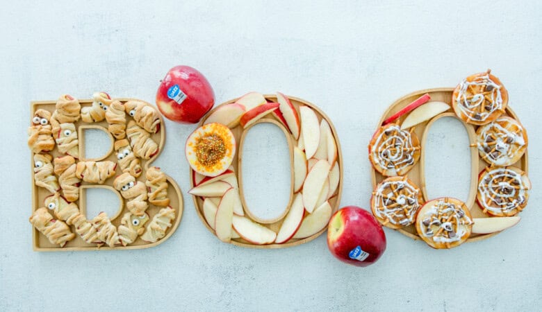 Halloween board spelling BOO with apple slices, cinnamon rolls, and mummies.