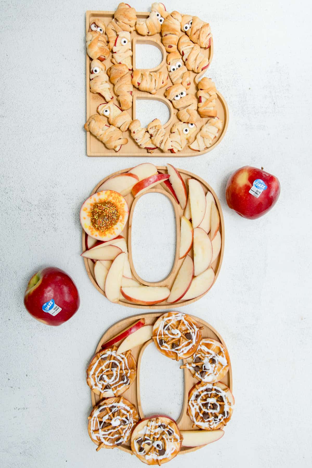 Halloween board spelling BOO with apple slices, cinnamon rolls, and mummies in a vertical display.