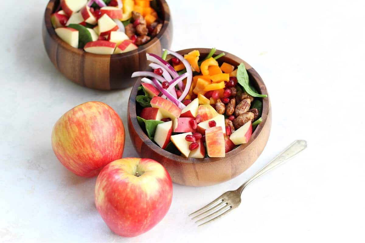 Salads served in wooden bowls and two sweet apples as sides.