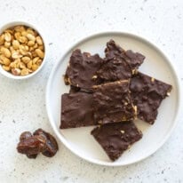 Upper view of some delicious date bars with peanuts coated in chocolate and peanuts on a bowl.