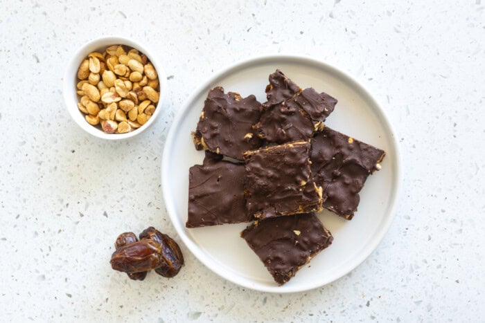 Upper view of some delicious date bars with peanuts coated in chocolate and peanuts on a bowl.