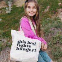 A little girl sitting over a fence holding a tote bag