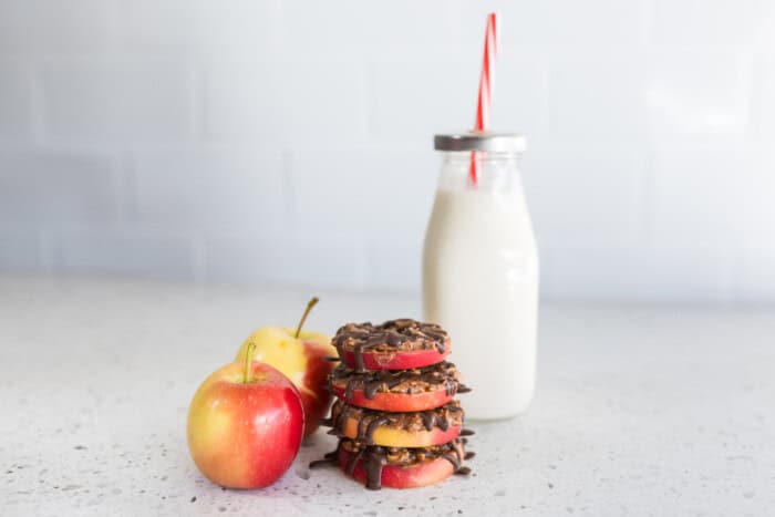 Healthy apple snacks are stacked next to two small apples and milk.