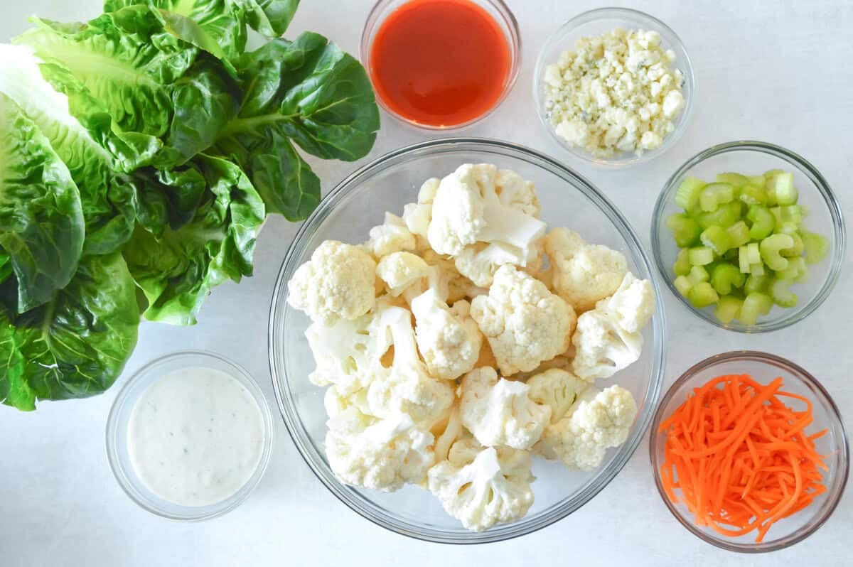 Buffalo Lettuce Wraps Ingredients for buffalo cauliflower lettuce wraps including cauliflower, lettuce, buffalo sauce, ranch dressing, celery, carrots, and cheese.