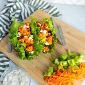 Buffalo cauliflower lettuce wraps served on a wooden board with sliced celery, shredded carrots, and ranch dipping sauce.