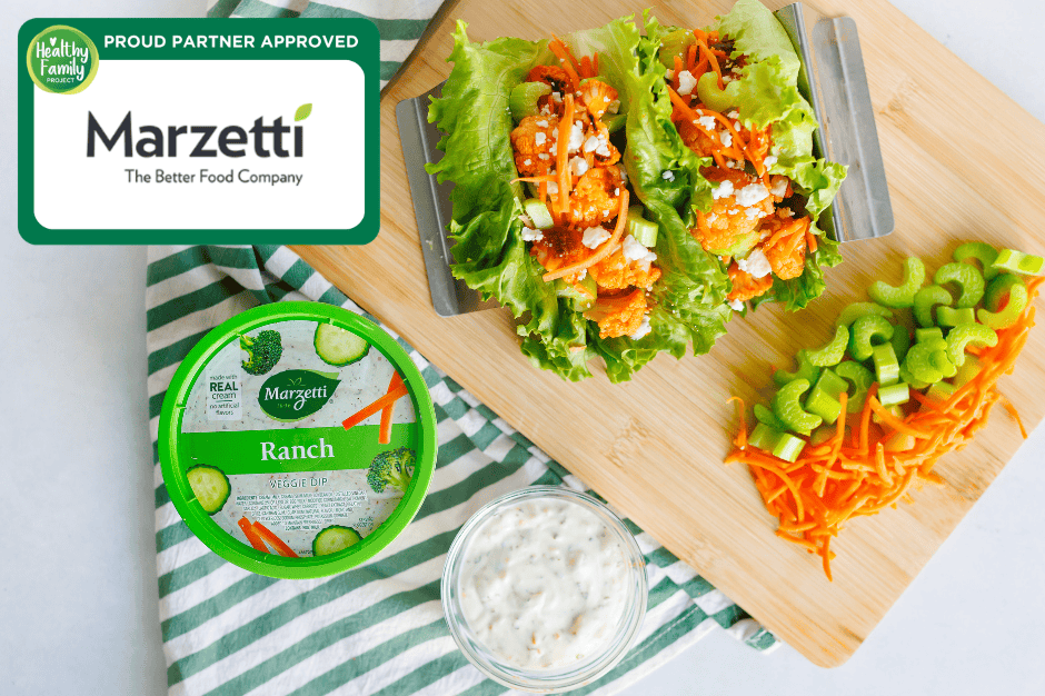 Buffalo Lettuce Wraps Buffalo cauliflower lettuce wraps topped with carrots, celery, and cheese, served with Marzetti ranch dip and fresh veggies on a cutting board.