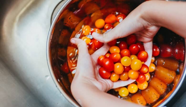 Close-up of hands rinsing Sunset® Sprinkles teeny tiny tomatoes in a large bowl of water over a kitchen sink.