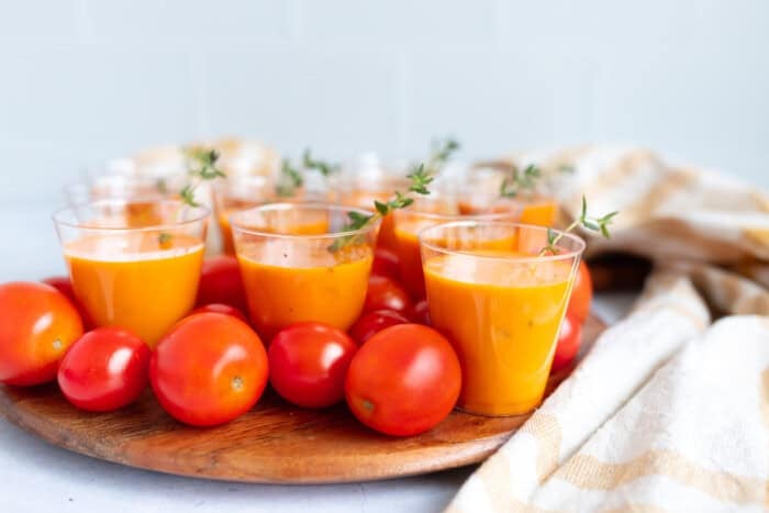 Mini tomato soup shooters in small glass cups, garnished with basil for a festive, healthy holiday appetizer.