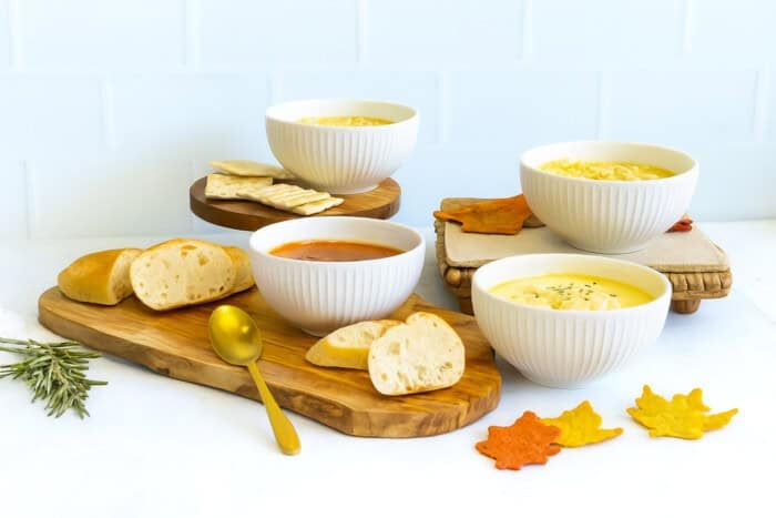 Thanksgiving soup bar with tomato soup, creamy chicken soup and noodle soup served with bread, crackers and fall shaped chips.