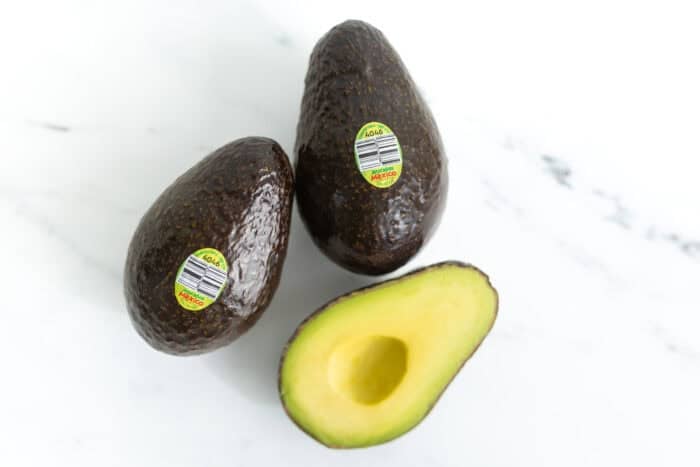 Fresh whole and halved avocados on white surface for easy avocado breakfast ideas
