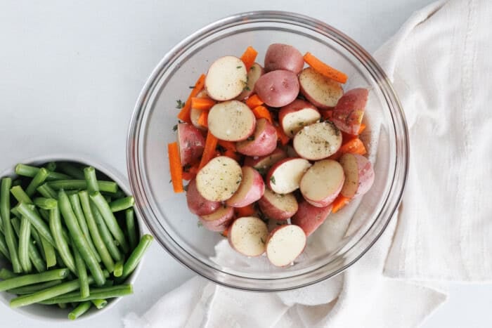 Baby potatoes and carrots tossed with oil and seasoning in a bowl, ready to roast with green beans