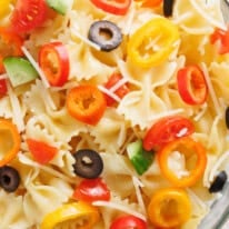 Close-up of rainbow Italian pasta salad with bowtie pasta, mini sweet peppers, cherry tomatoes, cucumbers, olives, and shredded cheese