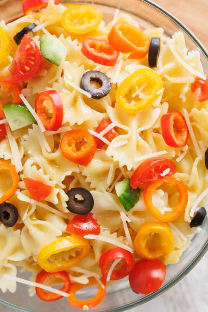 Close-up of rainbow Italian pasta salad with bowtie pasta, mini sweet peppers, cherry tomatoes, cucumbers, olives, and shredded cheese