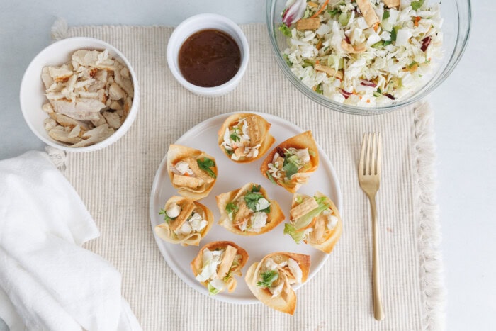 Baked chicken wonton cups with cabbage slaw served on a plate with dipping sauce and shredded chicken